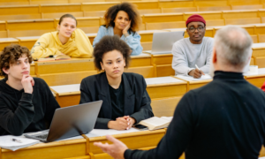 group of students in a lecture hall, attentively listening to an older male professor.