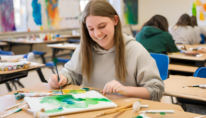 A girl smiling while doing her painting inside the classroom
