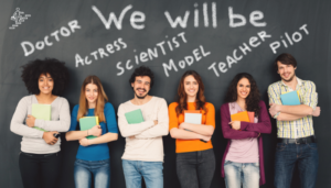 Six teens stand smiling in front of a chalkboard with career aspirations like Doctor and Scientist.