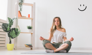 woman sitting on the floor meditating with a plan on the corner and a smiley face in the upper right  