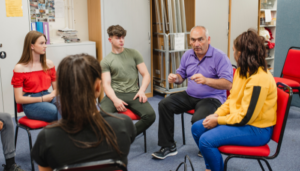 A group session with four teens and an older man in discussion.